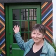 stadtrundgang_bild_selbitschka.jpg Frau in grüner Jacke präsentiert lachend eine rustikale Tür mit farbenfrohen Holzmuster.