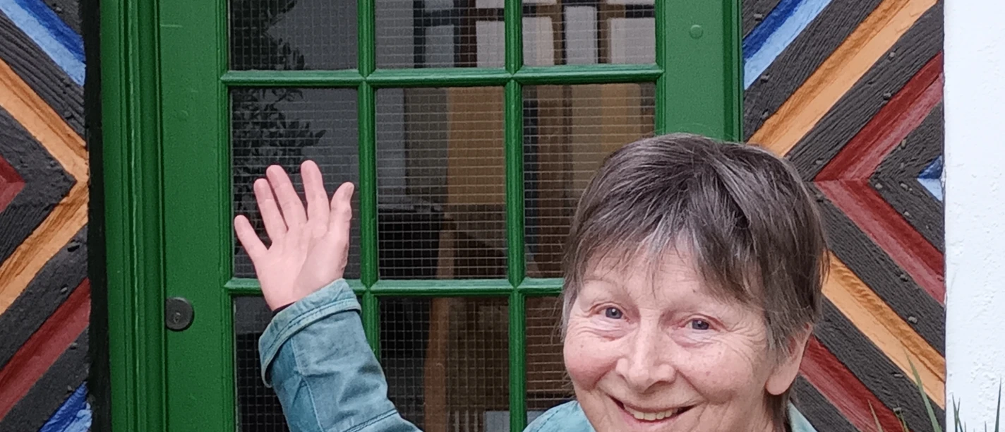 stadtrundgang_bild_selbitschka.jpg Frau in grüner Jacke präsentiert lachend eine rustikale Tür mit farbenfrohen Holzmuster.