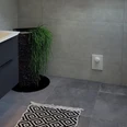 Modernes Badezimmer mit grauen Fliesen, schwarzem Waschbeckenunterschrank und dekorativem Teppich.