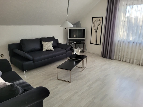Ein modernes Wohnzimmer mit schwarzen Sofas, stilvollem Couchtisch und hellem Laminatboden.