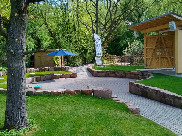 schoepfungsgarten_c_team_schoepfungsgarten (1).jpg Ein gepflegter Garten mit grünen Rasenflächen, bunten Sonnenschirmen und gepflasterten Wegen.