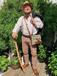 stadtfuehrer-900010141-22700-12.webp Älterer Mann in traditioneller Wanderkleidung mit Hut und Stock, umgeben von grüner Vegetation.
