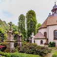 pfarrkirche_stockkaempen-900010262-22700-13.webp Historische Kapelle mit gepflegtem Friedhof, gesäumt von alten Grabsteinen und grüner Vegetation.