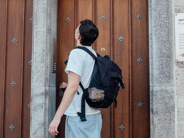 Mindwalk in Köln Ein junger Mann mit Rucksack betrachtet eine historische Holztür, daneben eine Banane als Wandkunst.