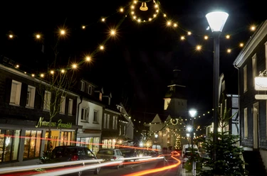 Eine festlich beleuchtete Straßenszene mit weihnachtlicher Dekoration am Abend, Menschen flanieren.