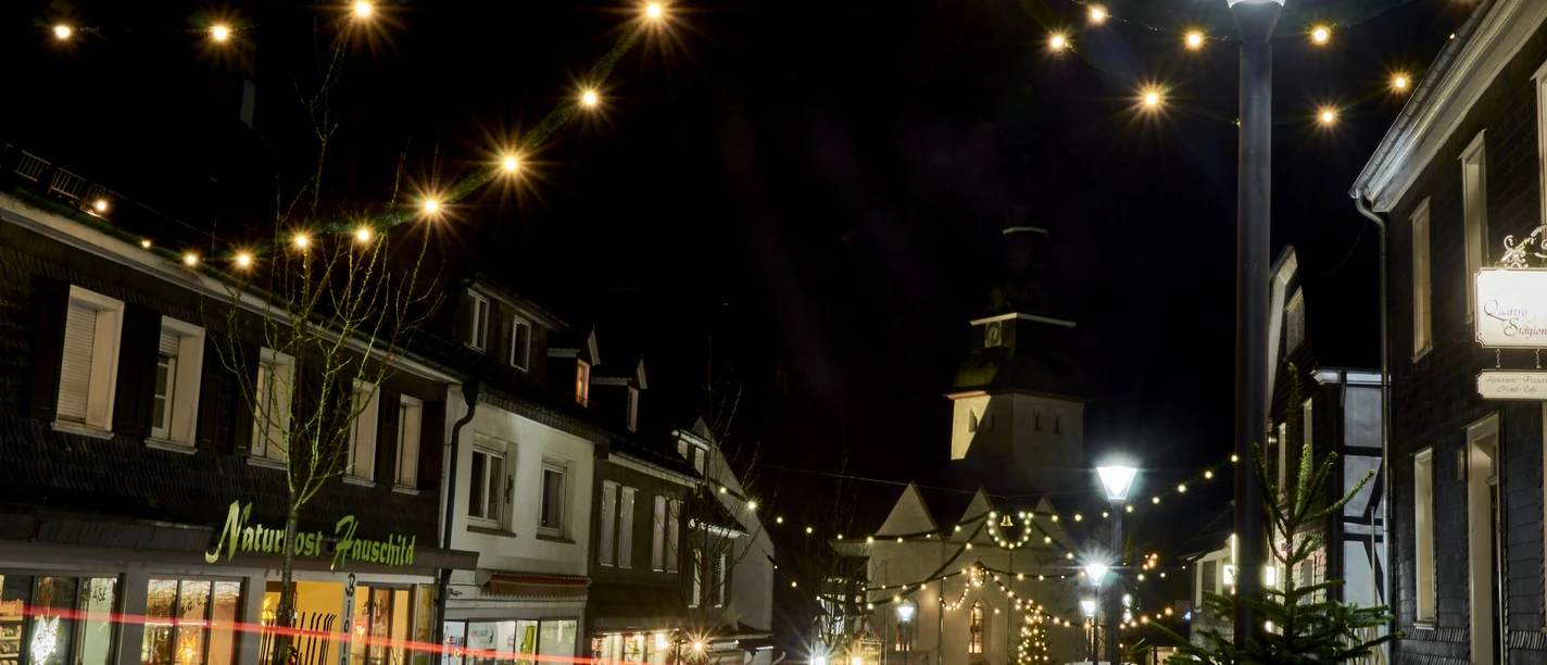 Eine festlich beleuchtete Straßenszene mit weihnachtlicher Dekoration am Abend, Menschen flanieren.
