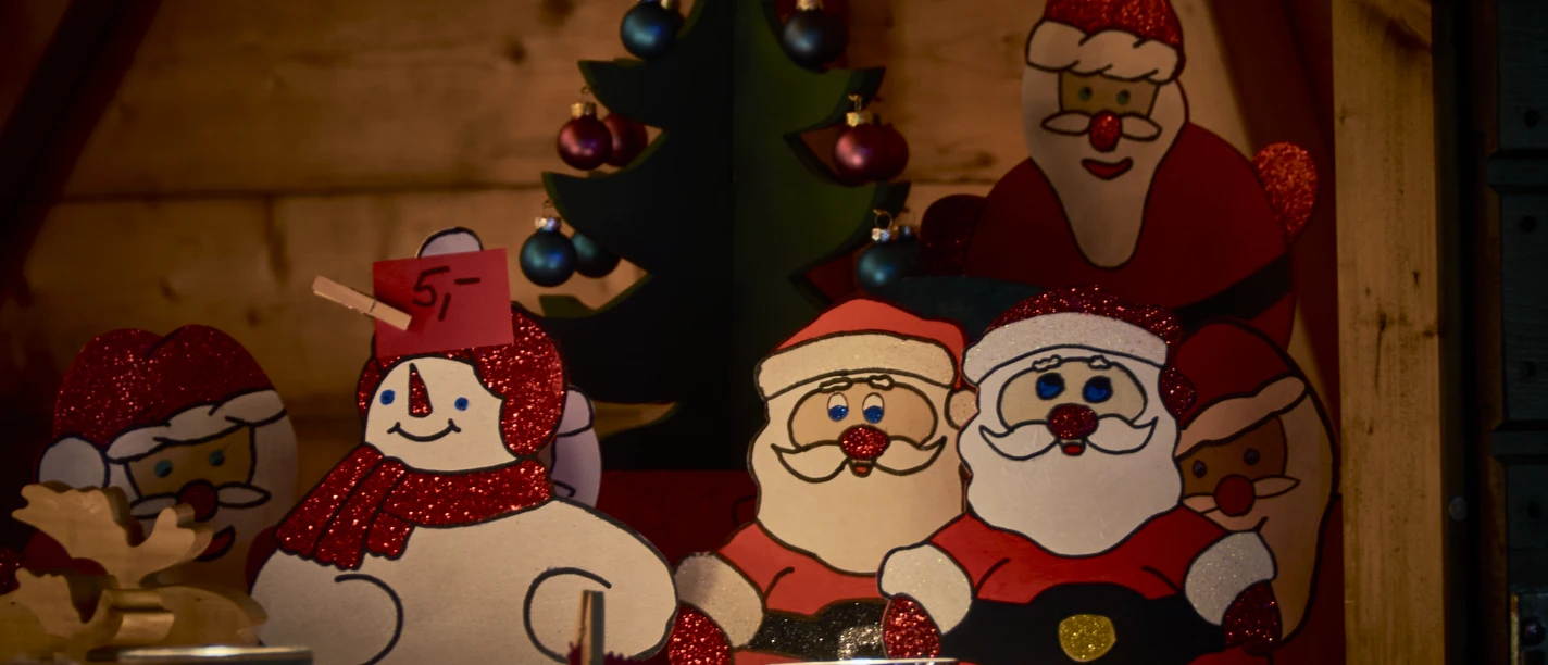 Weihnachtliche Holzfiguren, darunter Schneemänner und Weihnachtsmänner, umgeben von Kerzenlicht.
