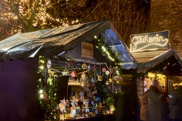 Weihnachtsmarkt Weihnachtsmarktstand bei Nacht mit leuchtender Dekoration, handgefertigten Holzartikeln und Lichtern.