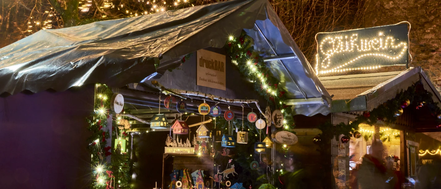 Weihnachtsmarkt Weihnachtsmarktstand bei Nacht mit leuchtender Dekoration, handgefertigten Holzartikeln und Lichtern.