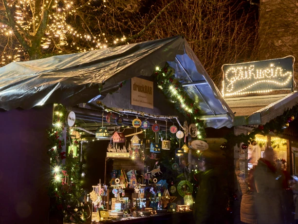 Weihnachtsmarktstand bei Nacht mit leuchtender Dekoration, handgefertigten Holzartikeln und Lichtern.
