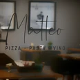 Blick in ein elegantes Restaurant mit dem Schriftzug "Matteo Pizza Pasta Vino" auf Glas.