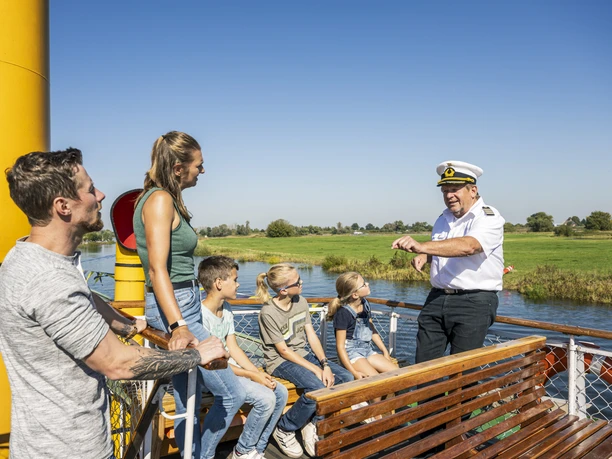 Buitendek van de raderstoomboot Kaiser Wilhelm Kapitein legt aan passagiers met kinderen uit hoe een raderstoomboot werkt