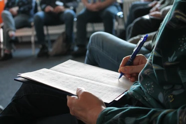 Teilnehmende:r an einem Workshop mit Stift und Papier auf einem Stuhl