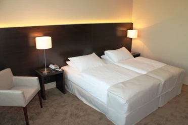 Superior twin room im relexa hotel Airport Düsseldorf-Ratingen.JPG Ein helles Hotelzimmer mit zwei Einzelbetten, zwei Nachttischen, Wandlampen und einem Sessel.