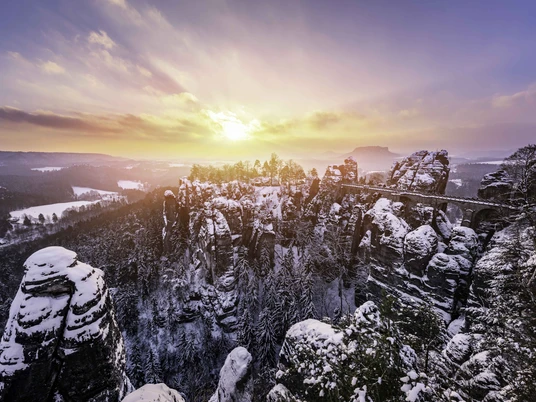 Basteibruecke_Winter_Blick_von_Ferdinandsaussicht_Kenny_Scholz_CC0_klein.jpg Schneebedeckte Felsen und Basteibrücke in winterlicher Landschaft im Sonnenuntergang.Snow-covered rocks and Bastei bridge in a wintry landscape at sunset.Zasněžené skály a most Bastei v zimní krajině při západu slunce.Pokryte śniegiem skały i most Bastei w zimowym krajobrazie o zachodzie słońca.Besneeuwde rotsen en de Bastei-brug in een winters landschap bij zonsondergang.Rocce innevate e ponte Bastei in un paesaggio invernale al tramonto.