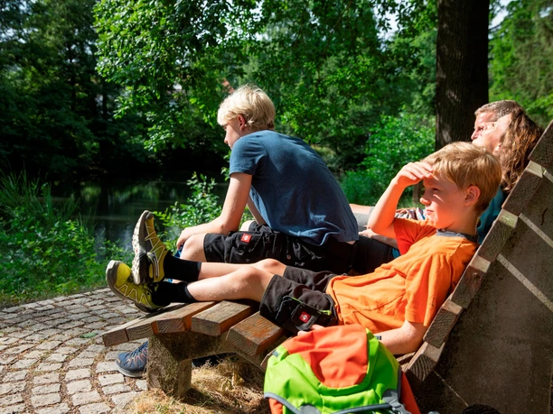 Familie sitzt auf einer Himmelsliege mit Blick auf Waldsee.