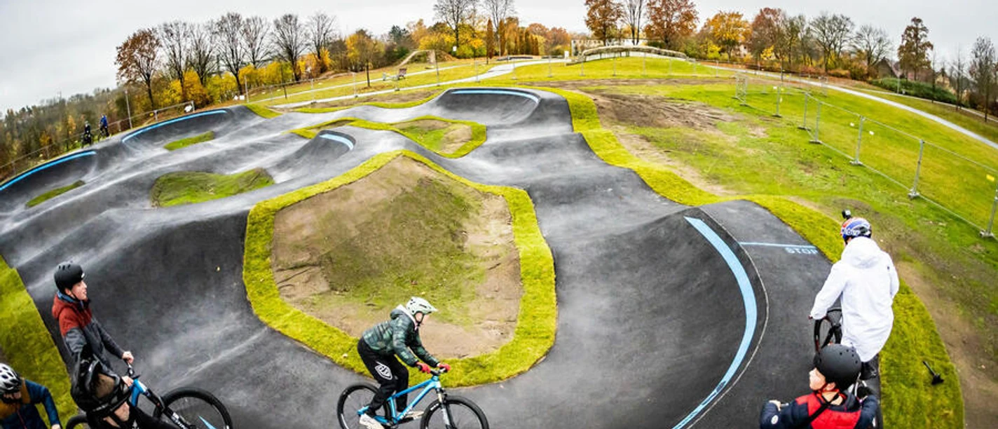 3467_811_1_g.JPG Ein geschwungener Pumptrack mit Radfahrern im herbstlichen Umfeld, umrahmt von Bäumen und Wiesen.
