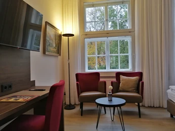 Helles Hotelzimmer mit zwei bequemen Sesseln vor einem Fenster, das einen Blick auf Bäume bietet.