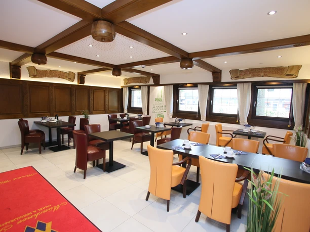 Moderner Frühstücksraum des Hotels mit Holzbalken, beige- und terrakottafarbenen Stühlen und großen Fenstern.