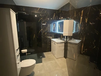 Ferienwohnungen "Orchideen Garten" - Bad/FeWo 1 Modernes Badezimmer mit dunklen Wänden, stilvollen Beleuchtung und weißen sanitären Einrichtungen.