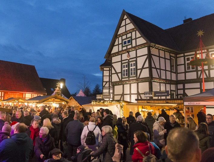 Menschenmenge besucht abendlichen Nikolausmarkt mit Fachwerkhäusern und festlich beleuchteten Ständen.