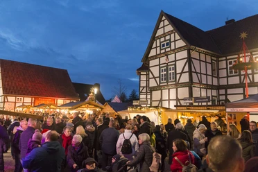 Menschenmenge besucht abendlichen Nikolausmarkt mit Fachwerkhäusern und festlich beleuchteten Ständen.