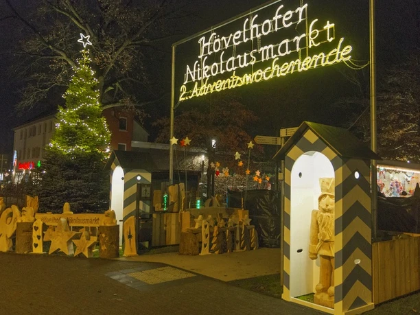 Weihnachtlich beleuchteter Nikolausmarkt in Hövelhof, festlich dekoriert mit Holzfiguren und Lichterketten.