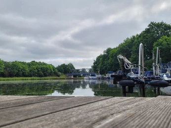 Hafen Getmold Ruhiger Hafen mit Anlegestellen und Booten an einem bewölkten Tag, im Hintergrund eine Brücke.