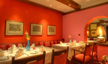 Modernes Restaurant mit roten Wänden, Kunstwerken und festlich gedeckten Tischen in warmem Ambiente.