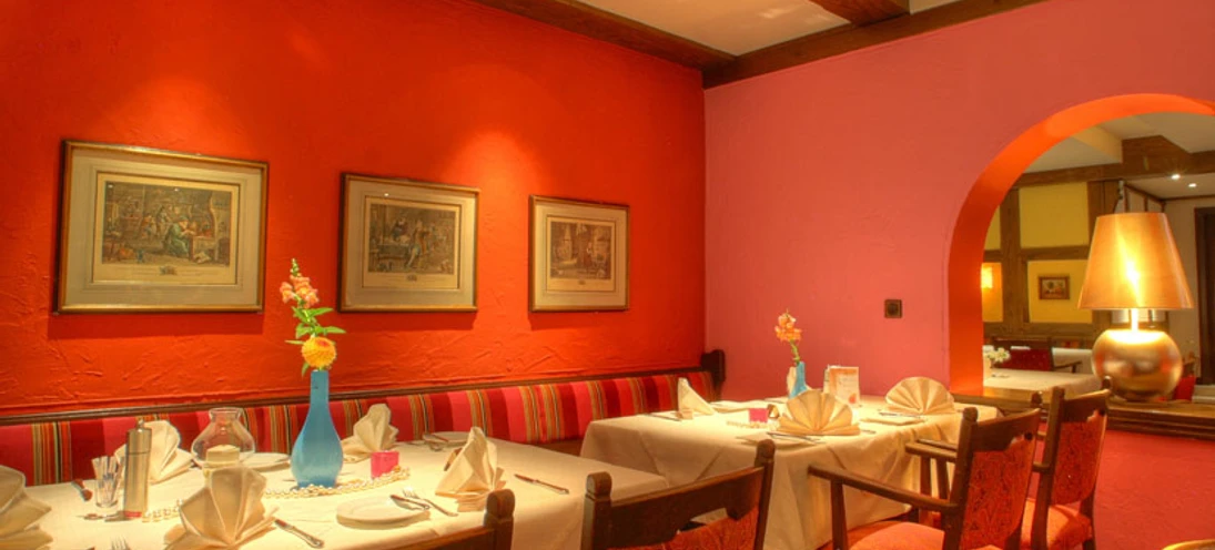 Modernes Restaurant mit roten Wänden, Kunstwerken und festlich gedeckten Tischen in warmem Ambiente.