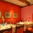 Restaurant Aureus im Hotel Vivendi-Herford (7).jpg Modernes Restaurant mit roten Wänden, Kunstwerken und festlich gedeckten Tischen in warmem Ambiente.