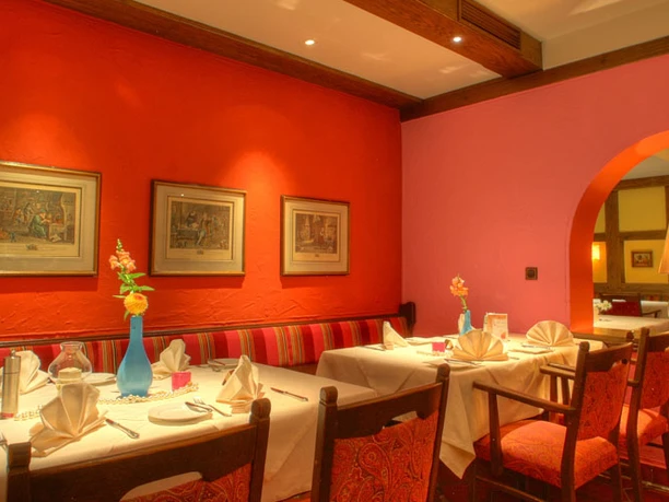 Restaurant Aureus im Hotel Vivendi-Herford (7).jpg Modernes Restaurant mit roten Wänden, Kunstwerken und festlich gedeckten Tischen in warmem Ambiente.