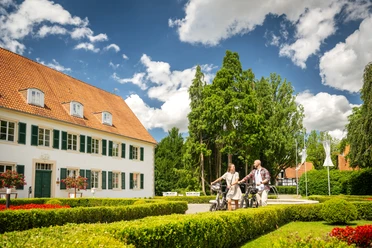 Kurpark Bad Holzhausen Zwei Personen radeln auf einem Weg im Kurpark Bad Holzhausen, umgeben von gepflegten Hecken und Bäumen.