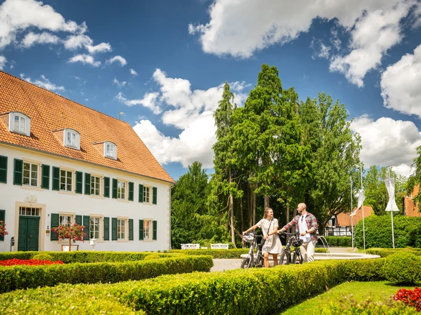 Kurpark Bad Holzhausen Zwei Personen radeln auf einem Weg im Kurpark Bad Holzhausen, umgeben von gepflegten Hecken und Bäumen.