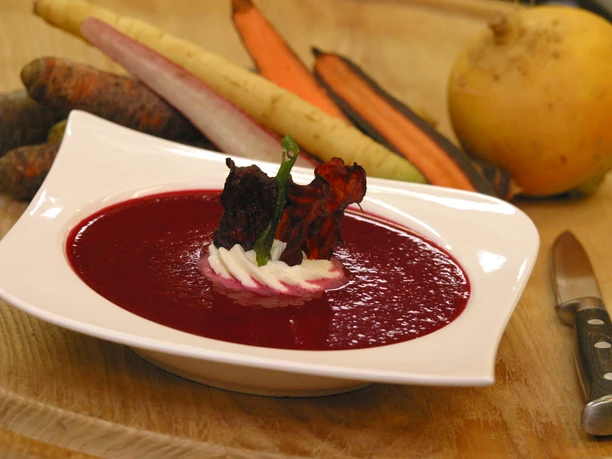 Eine weiße Schüssel mit Rote-Bete-Suppe, garniert mit Sahne und Rübenscheiben auf Holztisch.