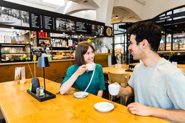 herford-markthalle-teutoburger-wald-tourismus-h-tornow-022-jpg.jpg Ein Mann und eine Frau genießen Kaffee an einem hellen Holztisch in einer modernen Markthallenatmosphäre.