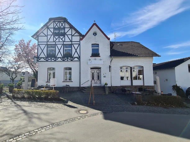 Café Die alte Schule Fachwerkhaus mit Restaurant „Alt-Kaster“ darunter, umgeben von blauer Himmel und leichten Wolken.