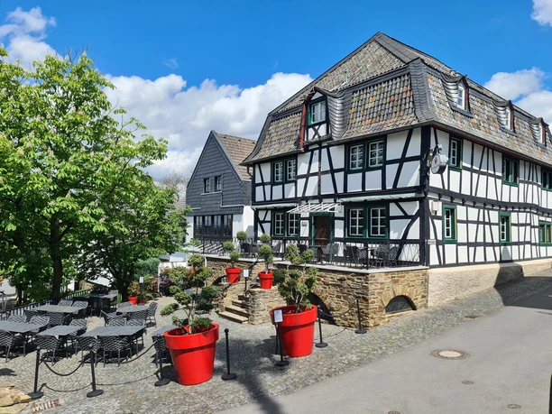Hotel Von Landsberg Traditionelles Fachwerkhaus mit Schieferdach umgeben von grünen Bäumen, roter Pflanzendekoration.