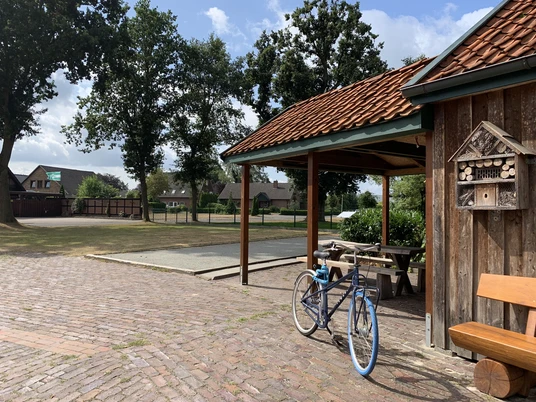 Hof Kleiberg Ein rustikaler Hof mit Holzgebäude, Fahrrad und Tisch in idyllischer ländlicher Umgebung bei Sonnenschein.