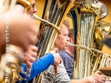 Musiker spielen in einer Reihe auf glänzenden Blechblasinstrumenten in einem Orchester.