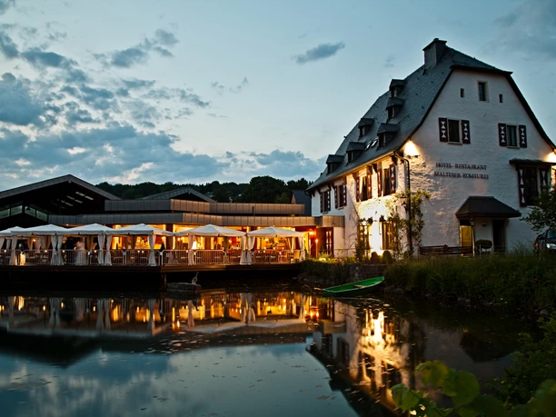 Malteser Komturei-1 Historisches Gebäude am Abend beleuchtet, spiegelt sich malerisch in einem ruhigen See wider.