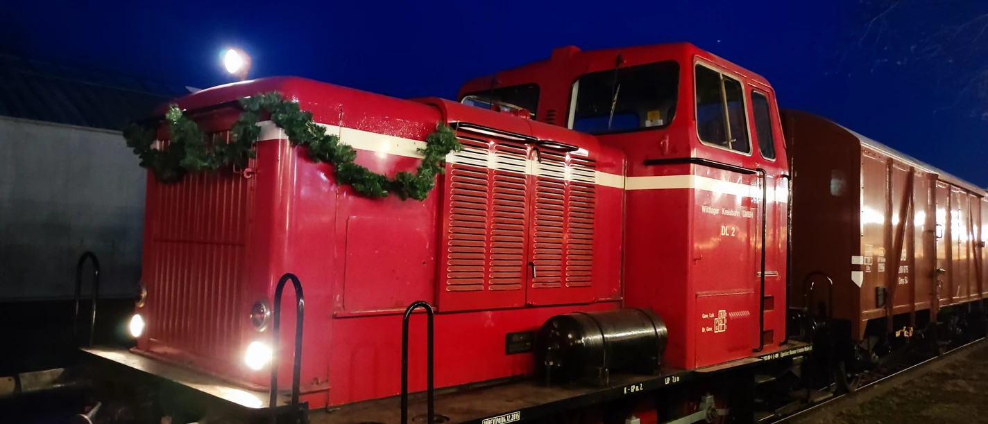 Rote Diesellokomotive der Museumseisenbahn Nikolaus, abends, mit Tannengirlande dekoriert.