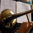 Posaunenchor Ein Posaunist spielt konzentriert, im Hintergrund sind Musiker und Notenblätter zu erkennen.