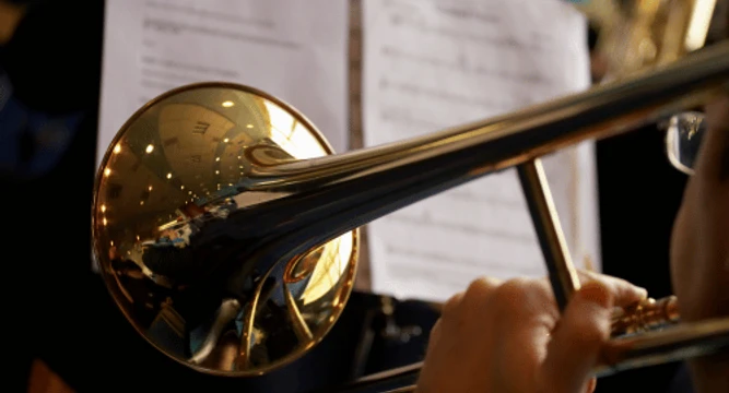 Posaunenchor Ein Posaunist spielt konzentriert, im Hintergrund sind Musiker und Notenblätter zu erkennen.