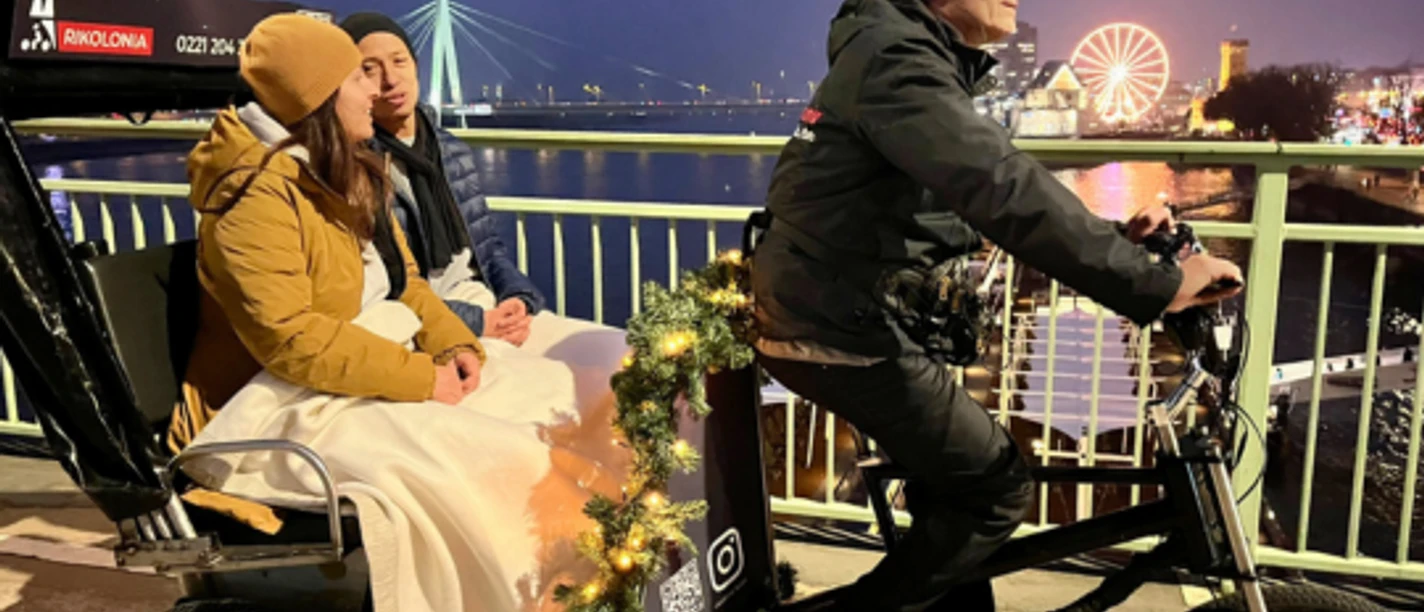 Rikolonia Köln Wintertouren II.png Rickshaw crosses a bridge over the Rhine and transports two people
