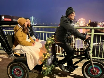 Rikolonia Köln Wintertouren II.png Rikscha fährt über eine Brücke über den Rhein und transportiert zwei PersonenRickshaw crosses a bridge over the Rhine and transports two people