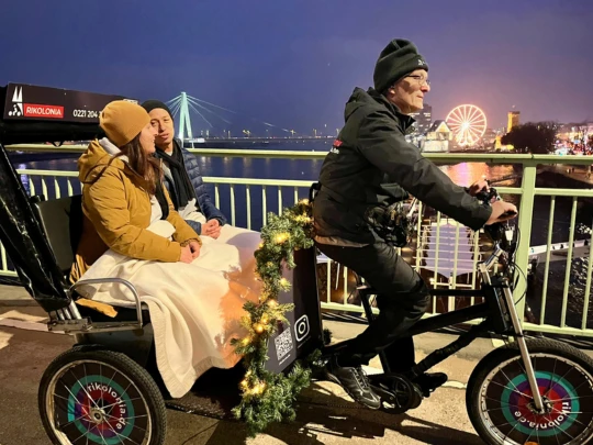 Rikolonia Köln Wintertouren II.png Rickshaw crosses a bridge over the Rhine and transports two people