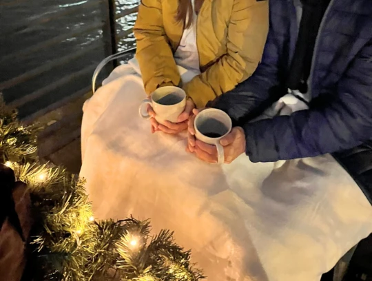 Rikolonia Rikscha Köln Glühweintour.png Zwei Personen sitzen hinten in einer Rikscha und halten Tassen mit Glühwein in der HandTwo people sit in the back of a rickshaw and hold cups of mulled wine in their hands