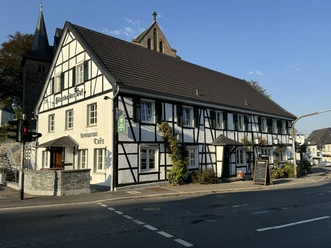 Dürscheider Hof - Außenansicht <p>Traditionelles Fachwerkhaus in Kürten bei Sonnenuntergang, im Hintergrund eine Kirche.</p>