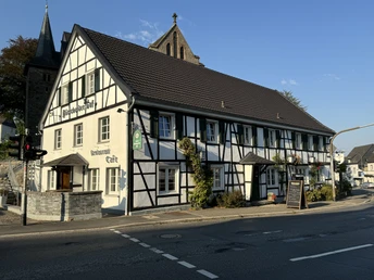 Dürscheider Hof - Außenansicht <p>Traditionelles Fachwerkhaus in Kürten bei Sonnenuntergang, im Hintergrund eine Kirche.</p>